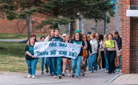 一群学生在校园里游行，举着一个标语，上面写着“全球网络赌博平台2024年夺回夜晚”。